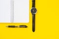 Notebook with ring binder with penand a wristwatch with leather straps, isolated on a yellow backdrop with copy space. Concept of