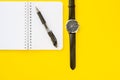 Notebook with ring binder with penand a wristwatch with leather straps, isolated on a yellow backdrop with copy space. Concept of