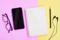 Notebook,Smartphone,Black pencil,Eyeglasses and Black Wired Earphones  on pink and yellow background Royalty Free Stock Photo