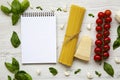 Notebook with spaghetti, parmesan, tomatoes, garlic and basil on white wooden background, top view. Royalty Free Stock Photo