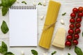 Notebook with spaghetti, parmesan, tomatoes, garlic and basil on white wooden background, top view. Copy space. Royalty Free Stock Photo