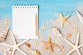 Notebook, starfishes and seashells on sand background top view. Planning summer holidays, trip, travel and vacation concept.
