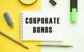 Notebook with text CORPORATE BONDS on office table with office supplies. Yellow color background