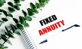 Notebook with text fixed annuity on white desk with pen and green plant decoration Royalty Free Stock Photo