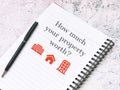 Notebook with text how much your property worth with a pen. Mortgage and real estate concept.