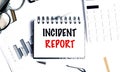 Notebook with text incident report on white desk with charts, keyboard, pen and glasses Royalty Free Stock Photo