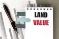 Notebook with the text land value on a desk with charts, a pen, and sticky bookmarks Royalty Free Stock Photo