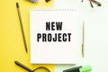 Notebook with text NEW PROJECT on office table with office supplies. Yellow color background Royalty Free Stock Photo