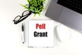 Notebook with text pell grant on white desk with laptop, pen, glasses, plant and mouse Royalty Free Stock Photo
