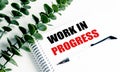 Notebook with text work in progress on white desk with green leaves and pen Royalty Free Stock Photo