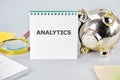 A notebook titled 'Analytics' sits next to a shiny piggy bank on a desk, showcasing a focus on data-driven