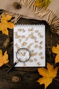 Notebook with wooden letters and a magnifying glass on a dark background with a scarf, plaid, around autumn yellow leaves and pine Royalty Free Stock Photo