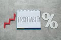 Notebook with word Profitability, percent symbol, up arrow on light grey table, top view. Profit concept