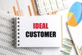 Notebook with the words ideal customer on desk with graphs, charts, pen and calculator, Royalty Free Stock Photo