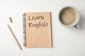 Notebook with words LEARN ENGLISH and cup of coffee on wooden background