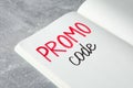 Notebook with words Promo Code on light grey table, closeup