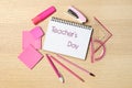 Notebook with words TEACHER`S DAY and set of pink stationery on wooden table, flat lay