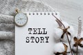 A notebook with the words TELL STORY on a light table, along with a branch of cotton and a clock. Natural light. Festive concept.