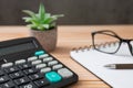 Notebooks, calculator, pens, glasses, cactus on wooden desks and loft walls with sunlight and copy space