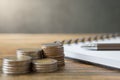 Notebooks, coins stack, pens on wooden desks and loft walls with sunlight and copy space Royalty Free Stock Photo