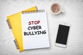 Notebooks with phrase STOP CYBER BULLYING and cup of coffee on table, flat lay