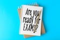 Notebooks with phrase ARE YOU READY FOR EXAMS and pencil on light blue background