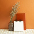 Notebooks and vase of misty blue dry flowers on beige ceramic mosaic tile desk. Orange background Royalty Free Stock Photo