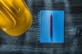 Notepad ballpoint pen hard hat on wooden board