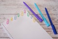 Notepad with blank page and colorful staples and blue pens on a wooden table. Mock up