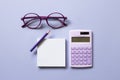 Notepad, colored pencil, calculator, glasses on purple background