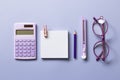 Notepad, colored pencil, cutter, calculator, glasses on purple background