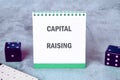 Notepad displaying capital raising concept alongside dice on a textured surface Royalty Free Stock Photo