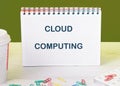 A notepad displaying the phrase cloud computing sits on a wooden desk with colorful paper clips and a coffee cup