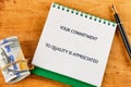 A notepad displays the message about commitment to quality. Nearby, a rolled banknote is tied with string, and a pen