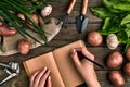 Notepad for entries in female hands, Close-up. Top view on a wooden background with garden tools, greens, onions, garlic