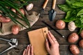 Notepad for entries in female hands, Close-up. Top view on a wooden background with garden tools, greens, onions, garlic