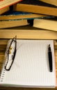 Notepad, fountain pen and glasses in front of books