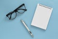 Notepad, glasses and pen on blue background. Office supplies or education concept. Top view with copy space. Royalty Free Stock Photo