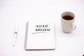 Notepad inscribed 2020 review with pen and tea cup on a white background