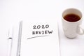 Notepad inscribed 2020 review with pen and tea cup on a white background
