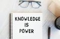 Notepad with the inscription KNOWLEDGE IS POWER. Paper cup with coffee and paper bag with breakfast on the table. View from above Royalty Free Stock Photo