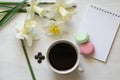 Notepad, macarons, cup of coffee and daffodils on a white table. Inspirational workplace.