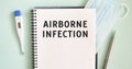 Notepad, medical mask, thermometer and pen on a blue background. AIRBORNE INFECTION text in a notebook