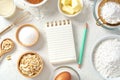 Notepad and pen for recipe with baking or cake ingredients in bowls, butter, milk, nuts and eggs with gold whisk on marble table