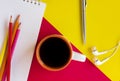 Notepad, pencils, coffee cup, headphones on the red and yellow background.