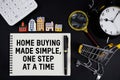 Notepad with the phrase Home Buying Made Simple, One Step At A Time surrounded by a pen, calculator, magnifying glass, clock, Royalty Free Stock Photo