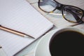 Notepad by reading glasses and coffee on table Royalty Free Stock Photo