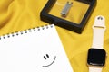 A notepad with a smiley face drawn on it and a smart watch with a flash drive. Modern new devices and emotions