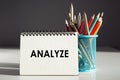 Notepad with text Analyze and blue pencil holder on dark grey background. Business concept Royalty Free Stock Photo