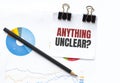 Notepad with text ANYTHING UNCLEAR on business charts and pen